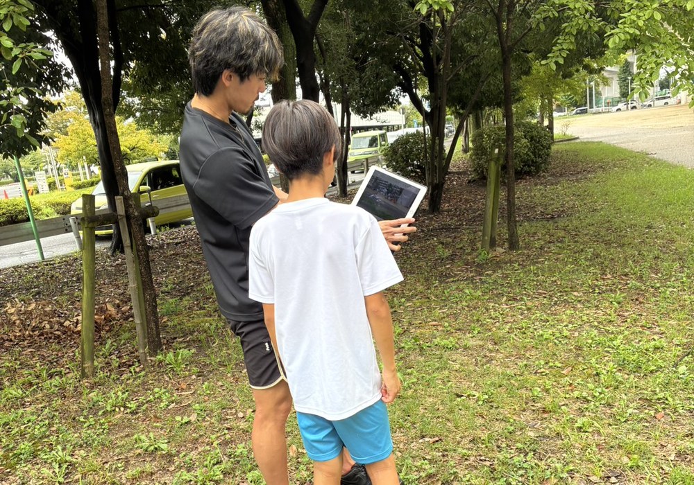 コーチがタブレットで走りの動画を見ながら指導する様子